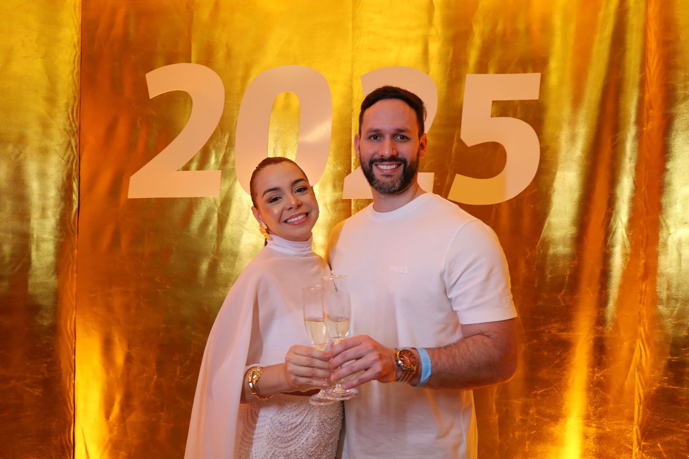 Casal brindando diante do painel dourado de 2025