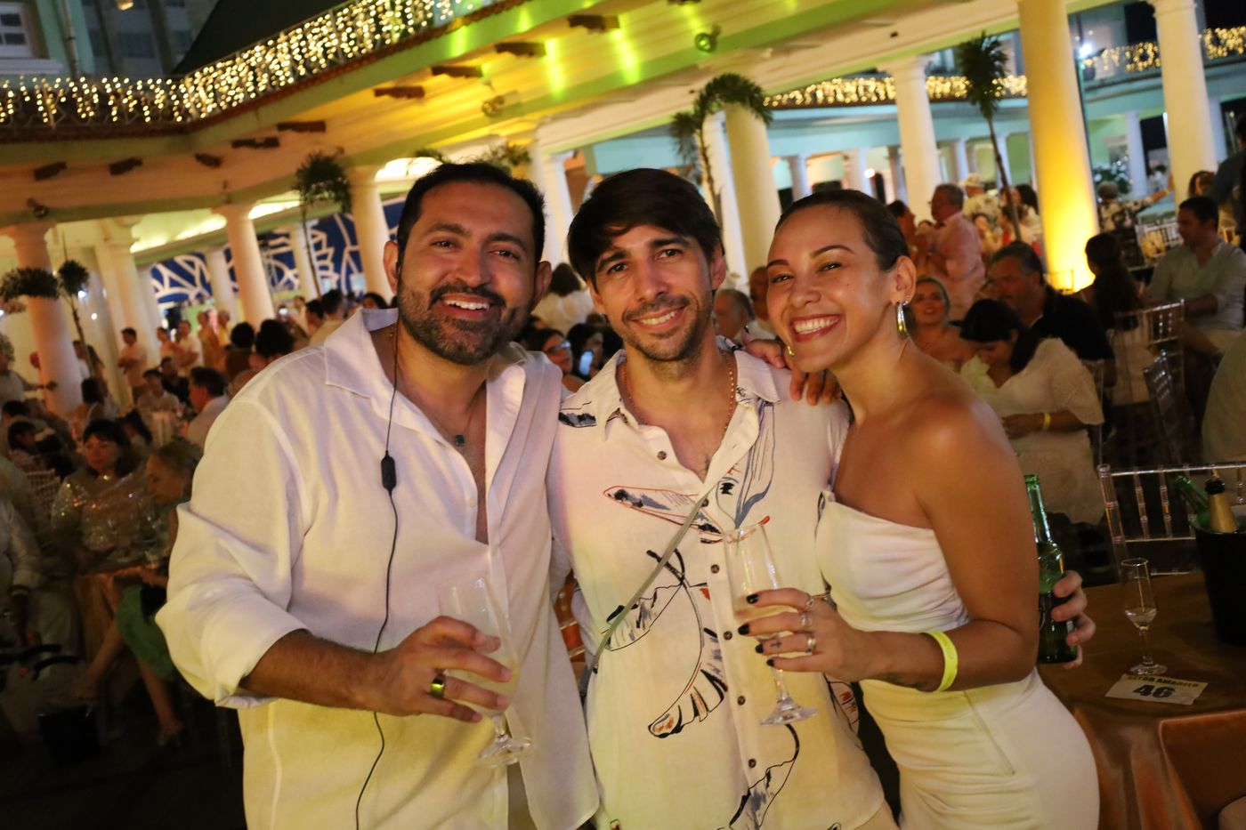 Amigos sorrindo na festa, com o salão cheio ao fundo